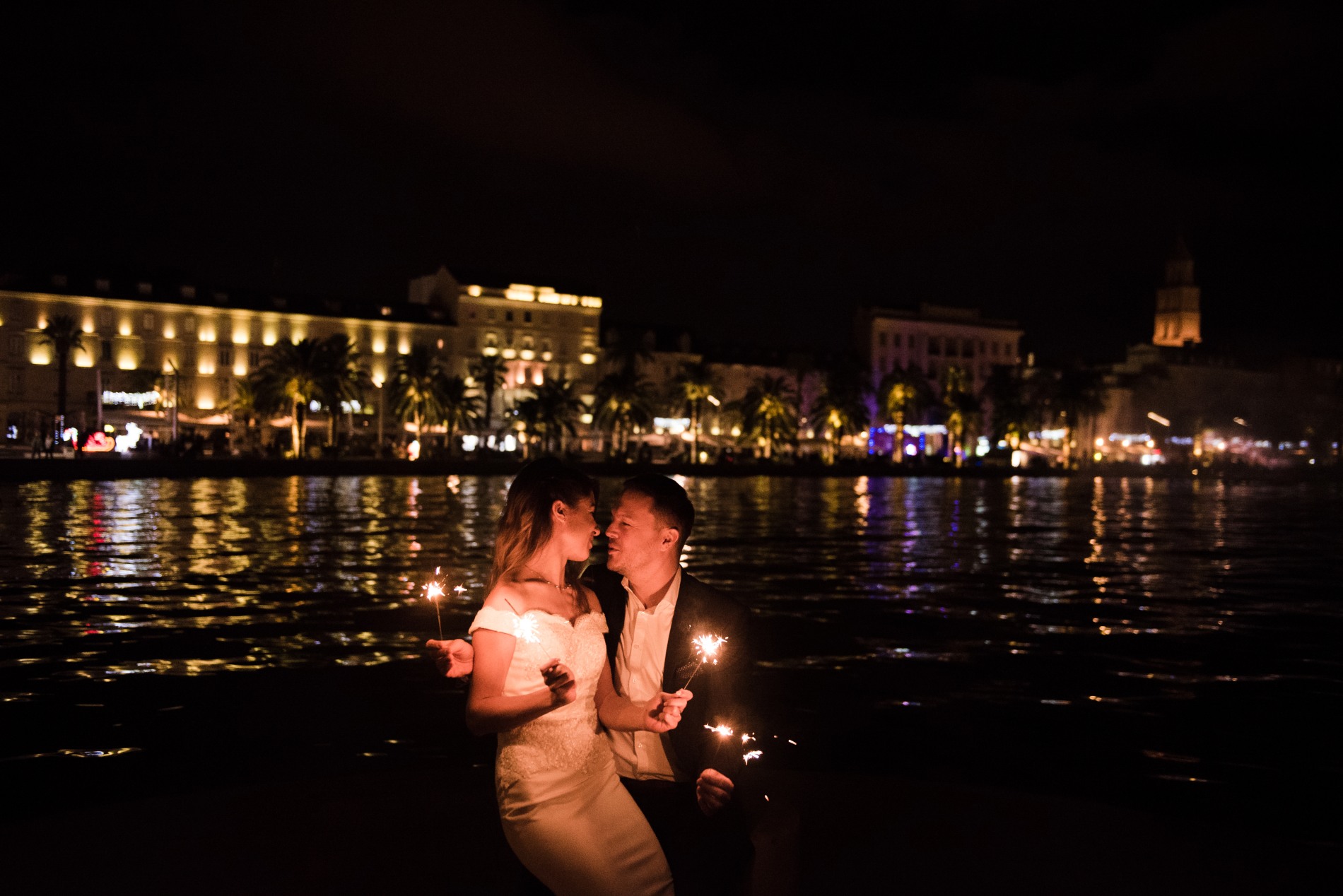 Bride sitting on grooms lap at night, holding flashers.